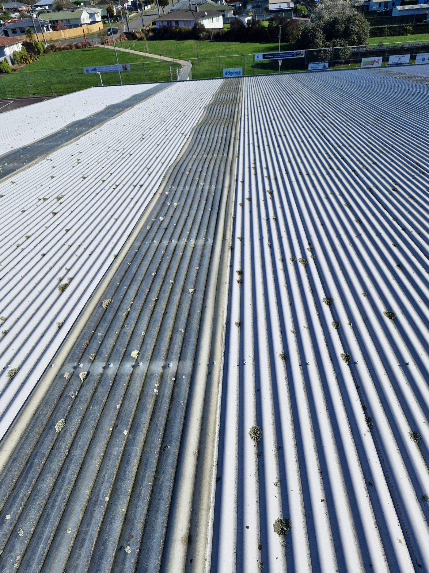 Lichen-spotted commercial roof at a sports ground before drone spray treatment, showing treated and untreated sections