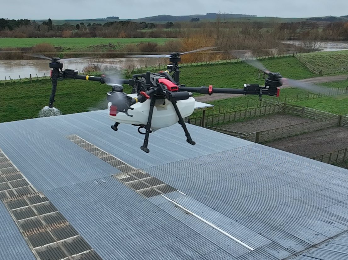 XAG spray drone applying moss and lichen treatment along the edge of a farm building roof
