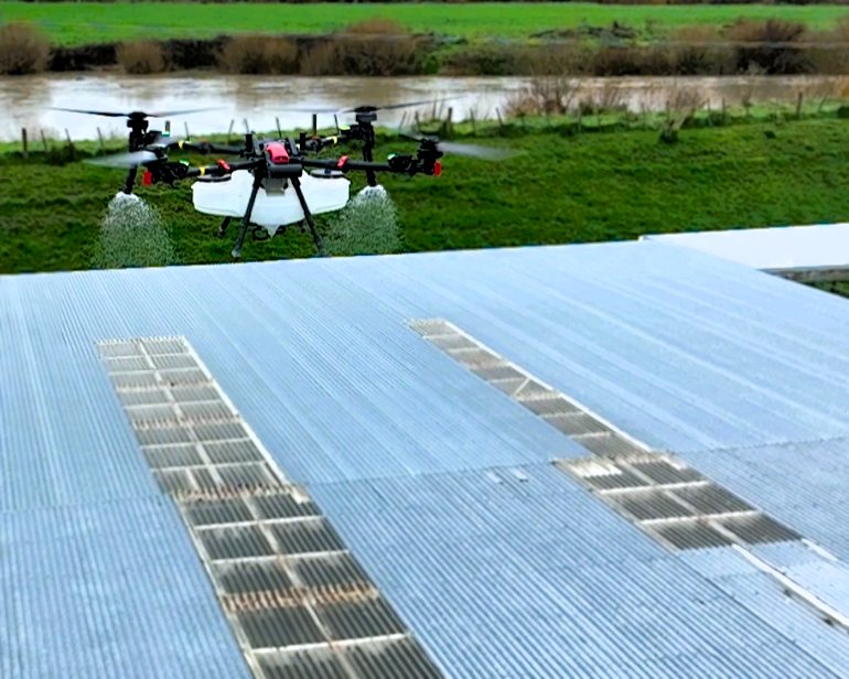 Drone spraying moss treatment across a long farm building roof